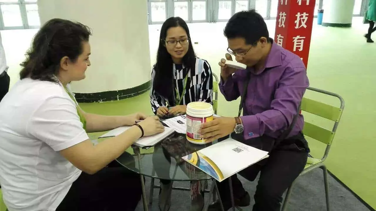 Interpreting at a Xiamen trade exhibition while an overseas buyer inspects a supplier's product sample